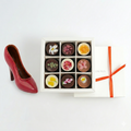 Box of chocolates with floral designs next to a red high-heeled shoe on a white background