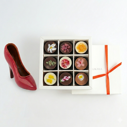 Box of chocolates with floral designs next to a red high-heeled shoe on a white background